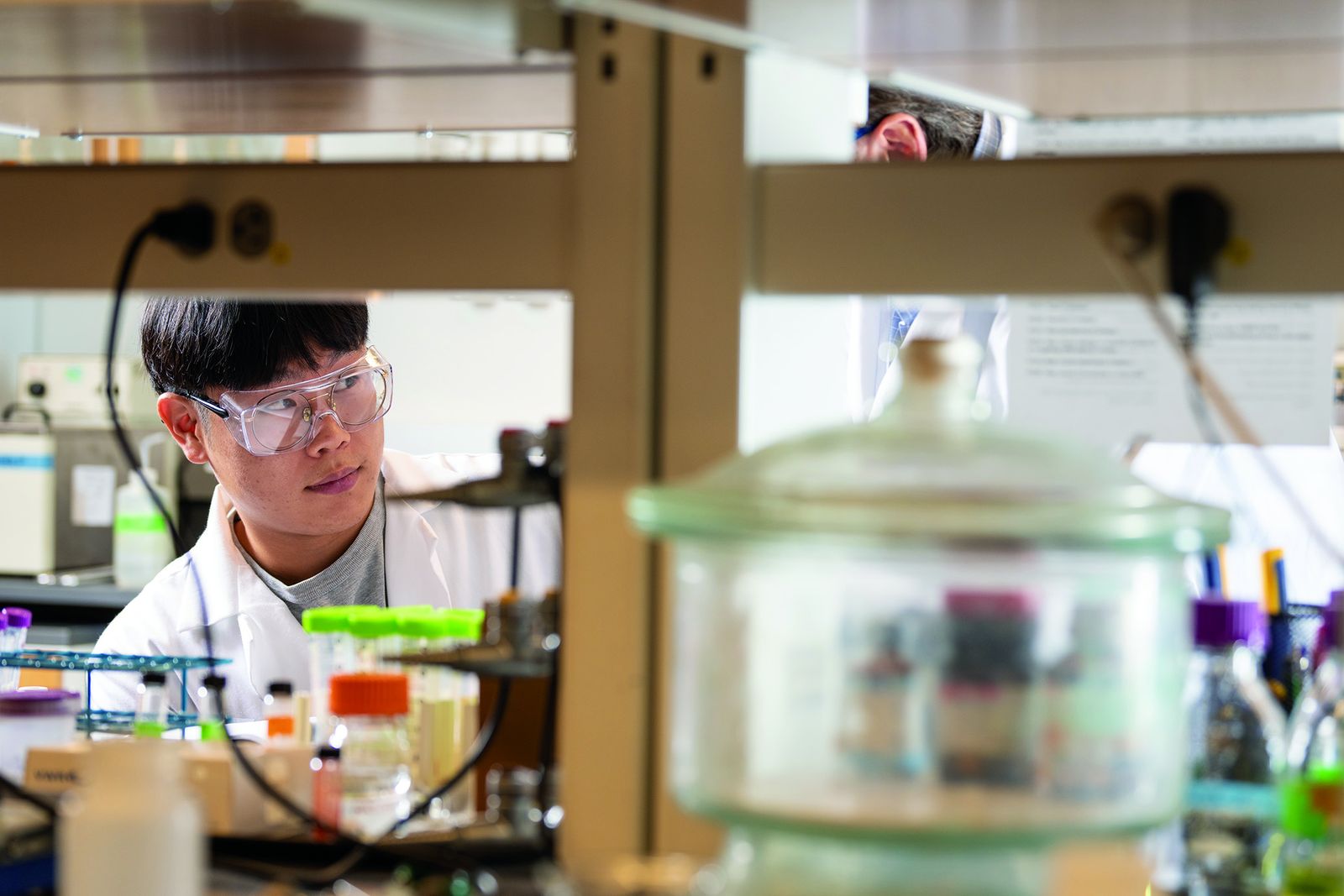 A Lehigh chemical engineering student in a lab coat and safety glasses working at a fume hood