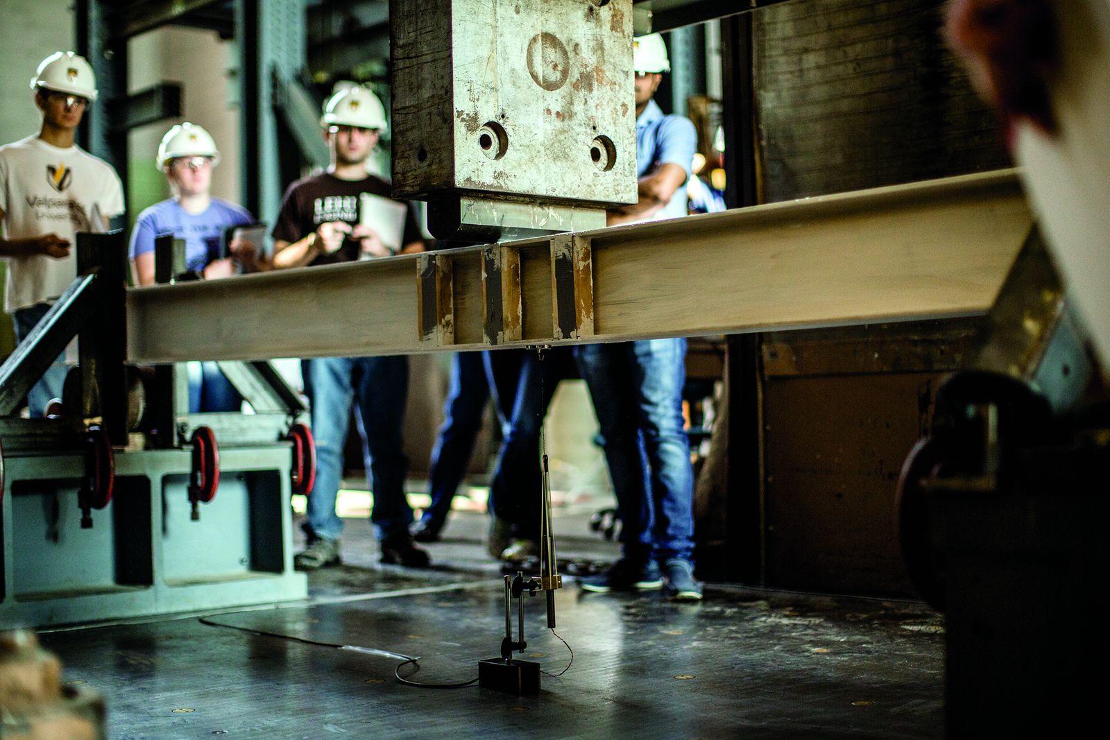 Lehigh students in hard hats observing a steel beam under load in Fritz Engineering Laboratory