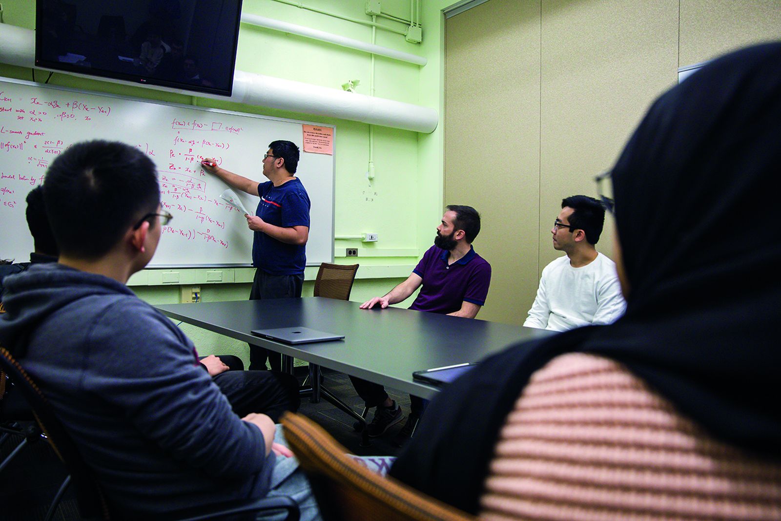 Frank E. Curtis working through optimization equations at a whiteboard with Lehigh graduate students