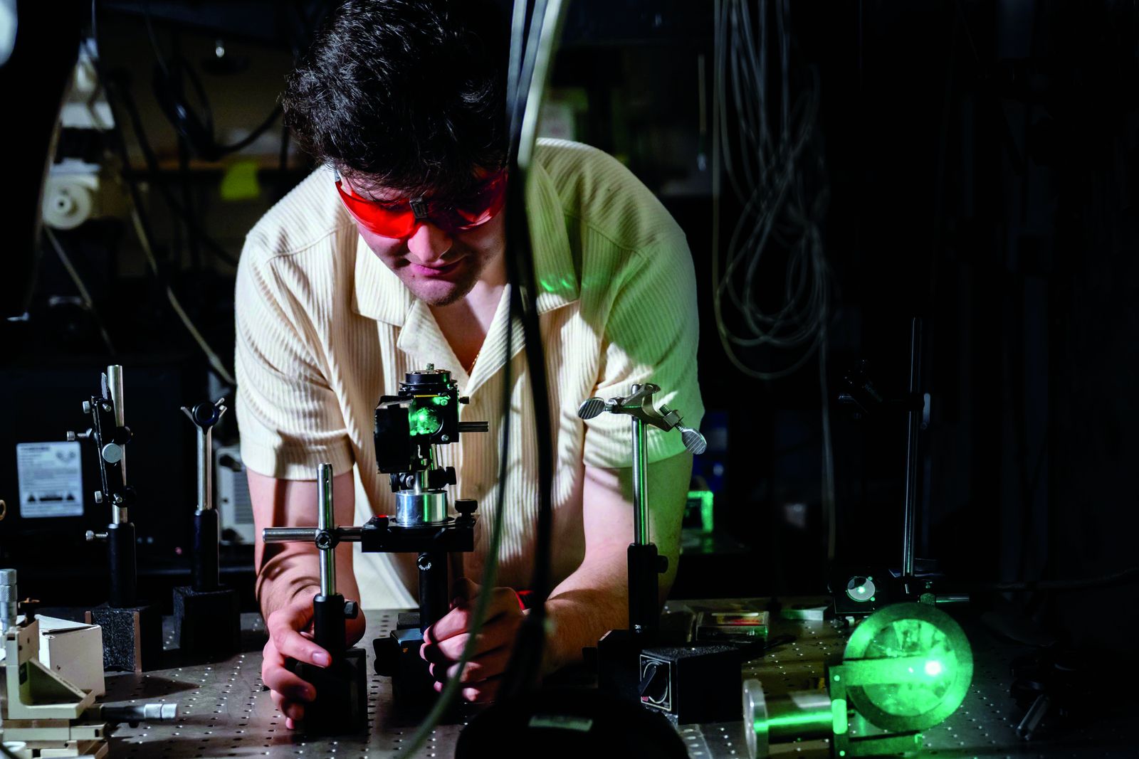 A Lehigh student in laser safety glasses aligning optics on a bench lit by a green laser