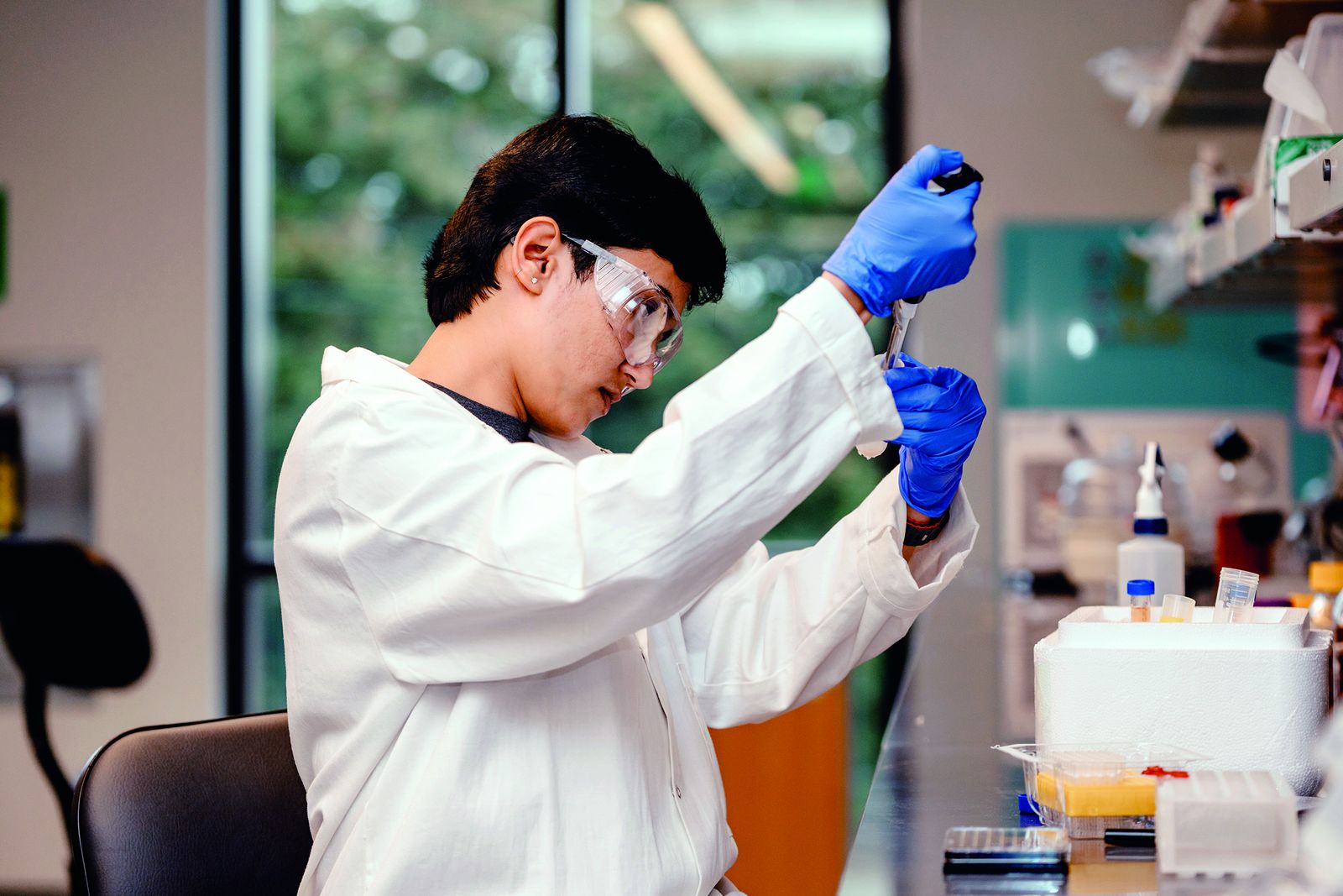 A Lehigh graduate student in a lab coat and safety goggles pipetting a sample in a polymer science laboratory