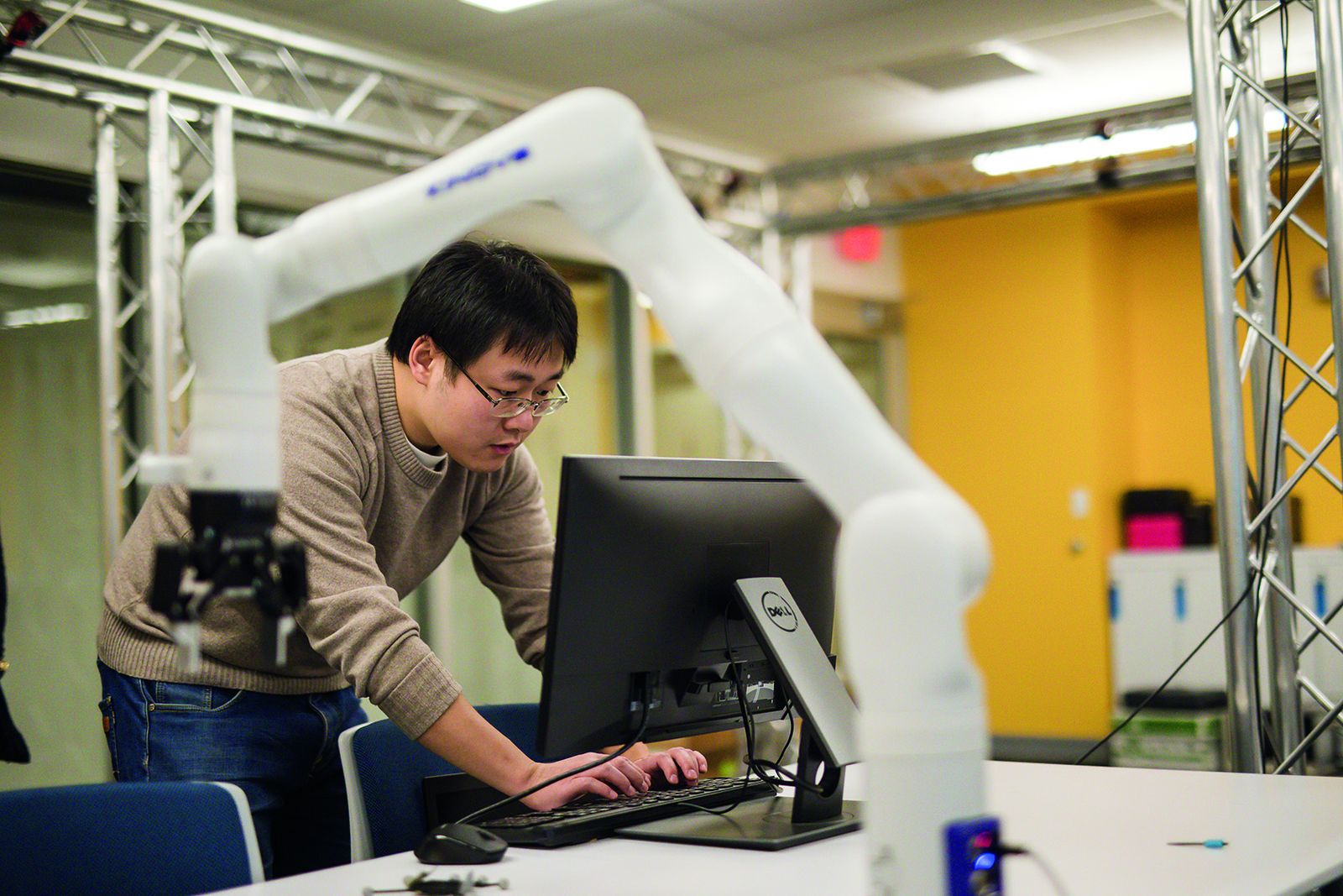 A Lehigh researcher at a workstation beside a robotic manipulator arm in Jeff Trinkle's robotics laboratory