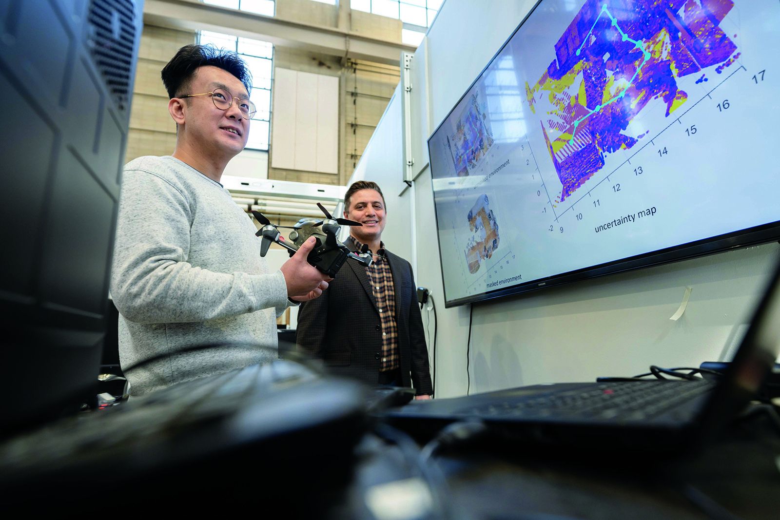Nader Motee holding an aerial drone in Lehigh's Autonomous and Intelligent Robotics laboratory, an uncertainty map on the screen behind