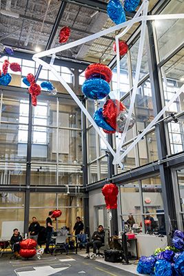 Interior of Lehigh’s Autonomous and Intelligent Robotics Laboratory with suspended red and blue robotic structures and people working below.