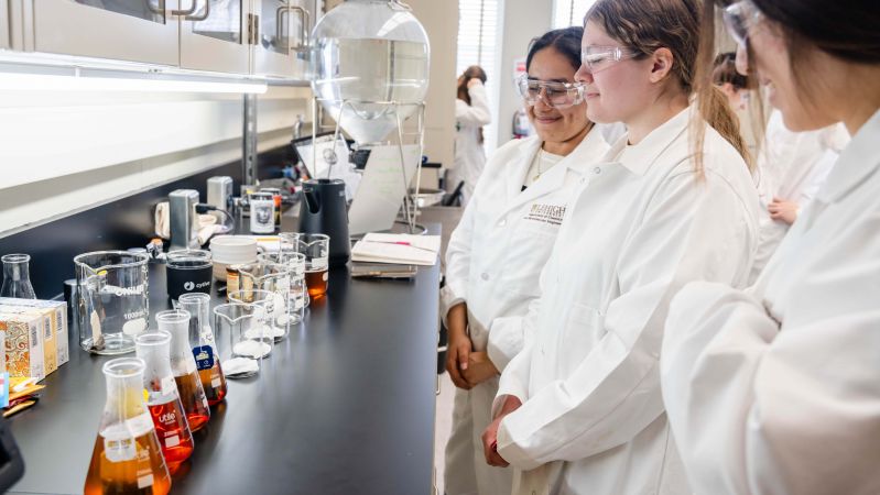 Students in lab coats observe brewing teas at a lab bench