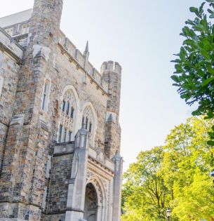Photograph of a gothic stone building and lush green trees on a bright, sunny day
