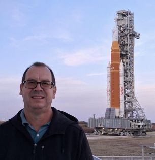 Mark Riddle in front the SLS rocket with the launchpad in the background.