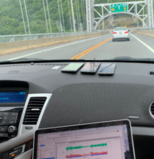 Photo from interior of car driving over a bridge with mobile phones on dashboard and a laptop screen