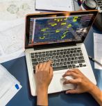 Hands working on laptop with papers on desk