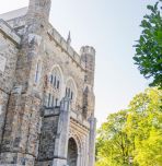 Photograph of a gothic stone building and lush green trees on a bright, sunny day