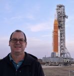 Mark Riddle in front the SLS rocket with the launchpad in the background.