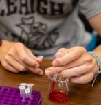 Detail image of student hands working with beaker for Purple Drop