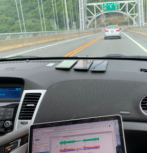 Photo from interior of car driving over a bridge with mobile phones on dashboard and a laptop screen